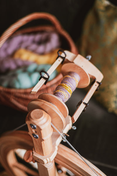 Kromski Sonata encore flyer. Wooden spinning wheel with yarn and a basket of yarn in the background