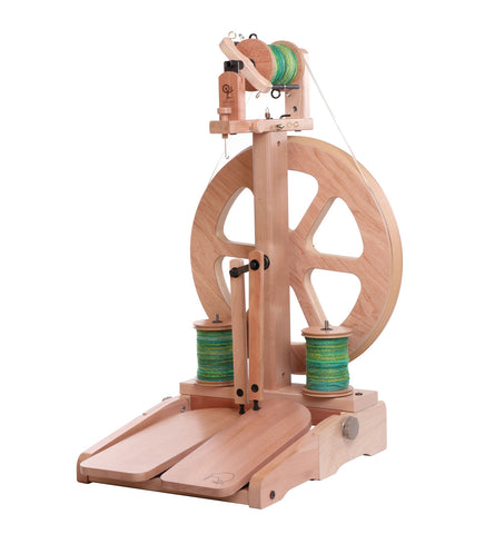 Ashford Kiwi 3 spinning wheel with folding treadles, timber veneered MDF wheel, and a three speed whorl. It is shown with green yarn on the bobbins and a natural wood finish.